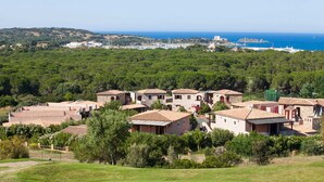 Un village côtier aux maisons aux toits de tuiles rouges, à la végétation luxuriante, offrant une vue sur la mer.