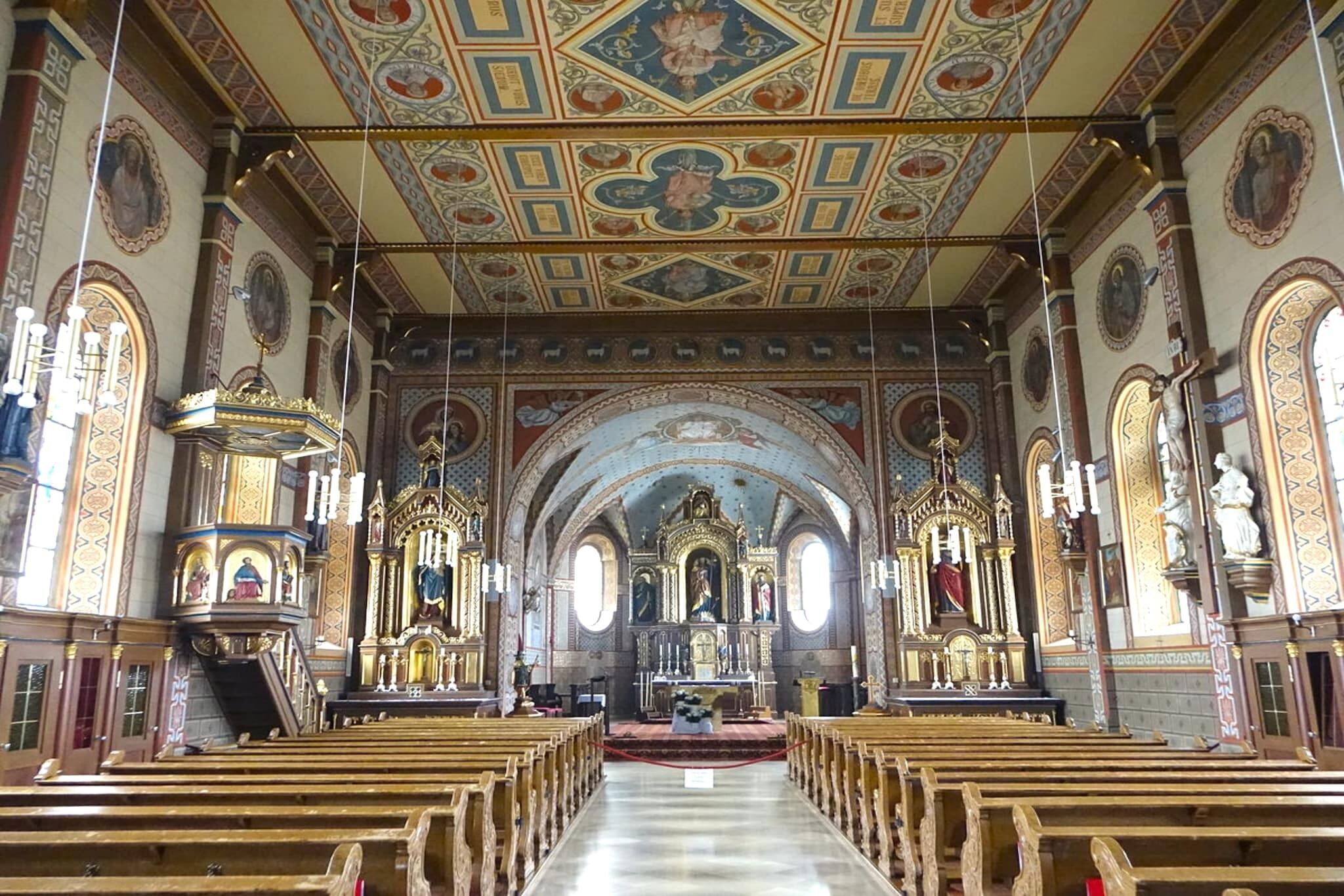 L’intérieur d’une église, avec ses bancs en bois, son autel central et ses décorations élaborées au plafond.