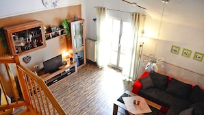 A living room with a wooden staircase, a sofa, a TV, and a bookshelf. - Apartment Near Kurpark Lake (Bodenmais)