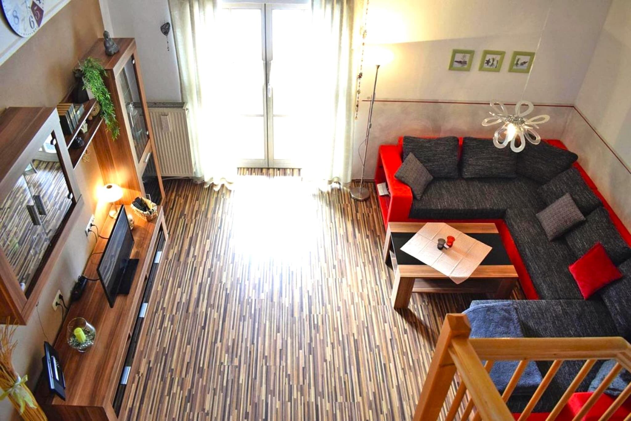 A modern living room with a wooden floor, a red sofa, a wooden coffee table, and a TV on a wooden stand.
