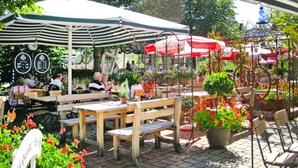 An outdoor café with wooden tables and benches, surrounded by potted plants and flowers. - Apartment Near Kurpark Lake (Bodenmais)