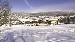 A snow-covered landscape with a large lodge featuring multiple buildings and a ski slope in the background. - Apartment Near Kurpark Lake (Bodenmais)