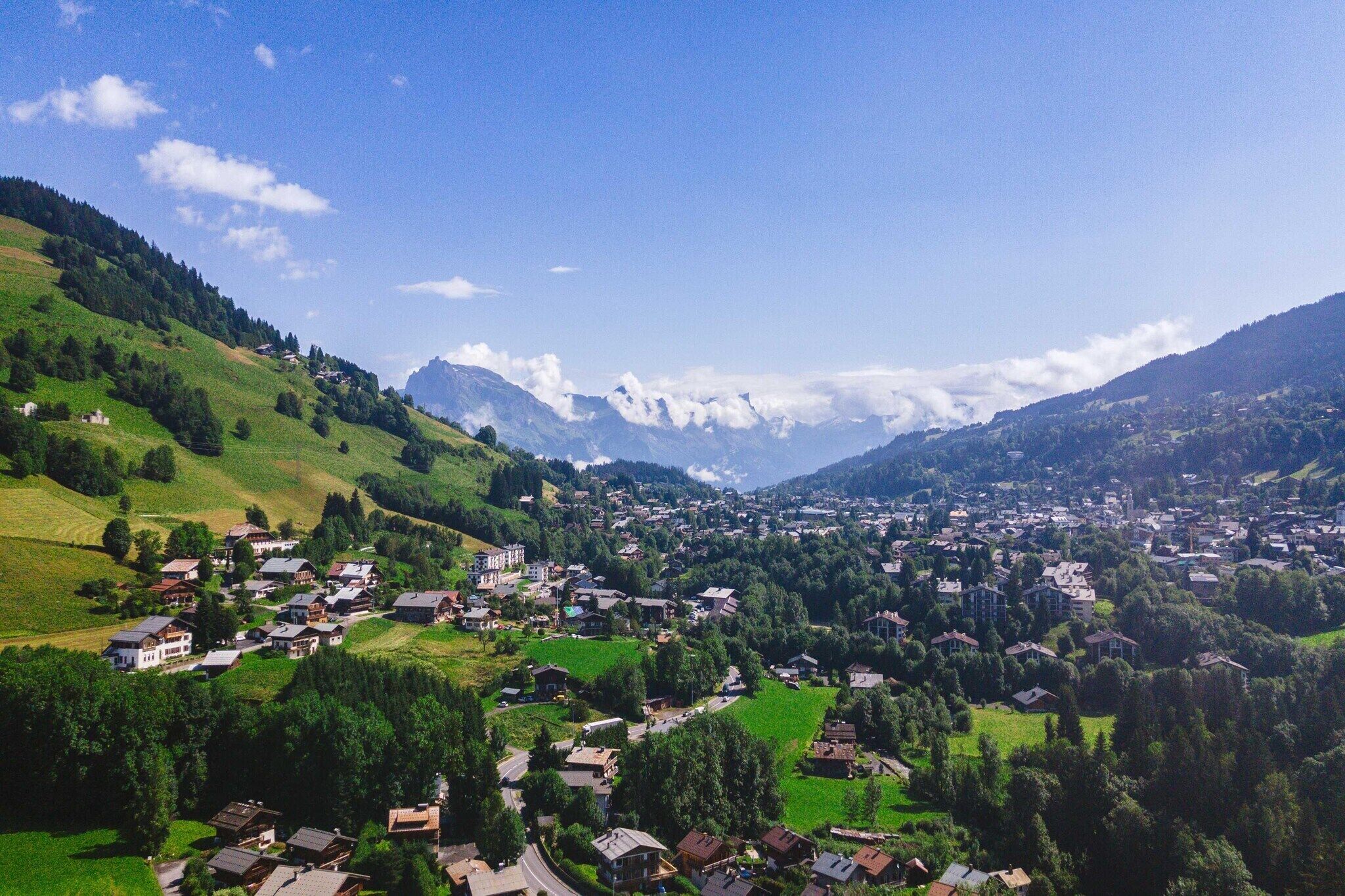 Ein dorf am Berg mit Häusern, die sich über das Tal verteilen, umgeben von üppiger Vegetation und fernen, schneebedeckten Gipfeln.