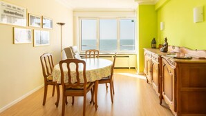 Un espace repas avec une table ronde, des chaises et une vue sur la mer grâce à de grandes fenêtres.