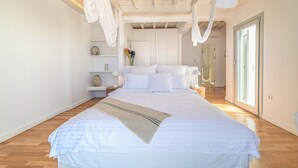A spacious bedroom with a large bed, wooden flooring, and a view of a bathroom. - Anthis Villa Poseidon, Private infinity Pool! (Mykonos)