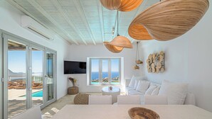 A modern living room with a large window, a TV, and a view of the sea. - Anthis Villa Poseidon, Private infinity Pool! (Mykonos)