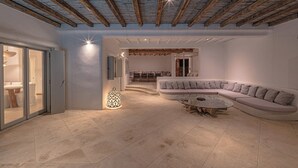 A spacious living area with a curved sectional sofa, a coffee table, and a dining area with a wooden table and chairs. - Anthis Villa Poseidon, Private infinity Pool! (Mykonos)