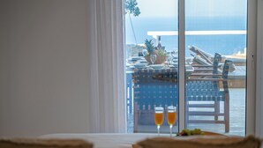 A hotel room with a view of the sea, a dining table set with plates and glasses, and a fruit bowl on the windowsill.