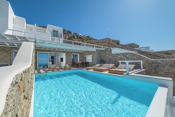 A clear blue pool with lounge chairs and a stone wall backdrop.