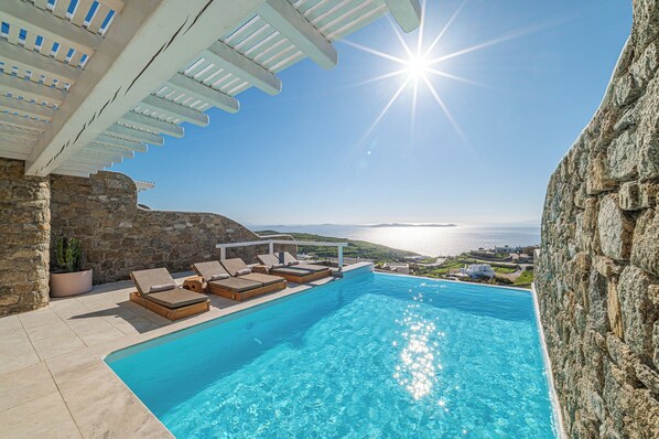 A pool area with lounge chairs and a view of the sea.