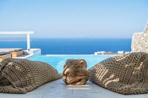 Zona junto a la piscina con vista al mar, que incluye dos espacios amplios con asientos texturizados y una escultura de piedra.