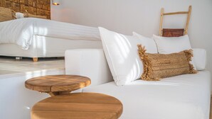 Una camera d'albergo moderna con un divano bianco, uno sgabello di legno e un letto con lenzuola bianche.