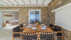 Zona pranzo con parete in pietra, tavolo in legno apparecchiato per sei e vista attraverso una porta in vetro.