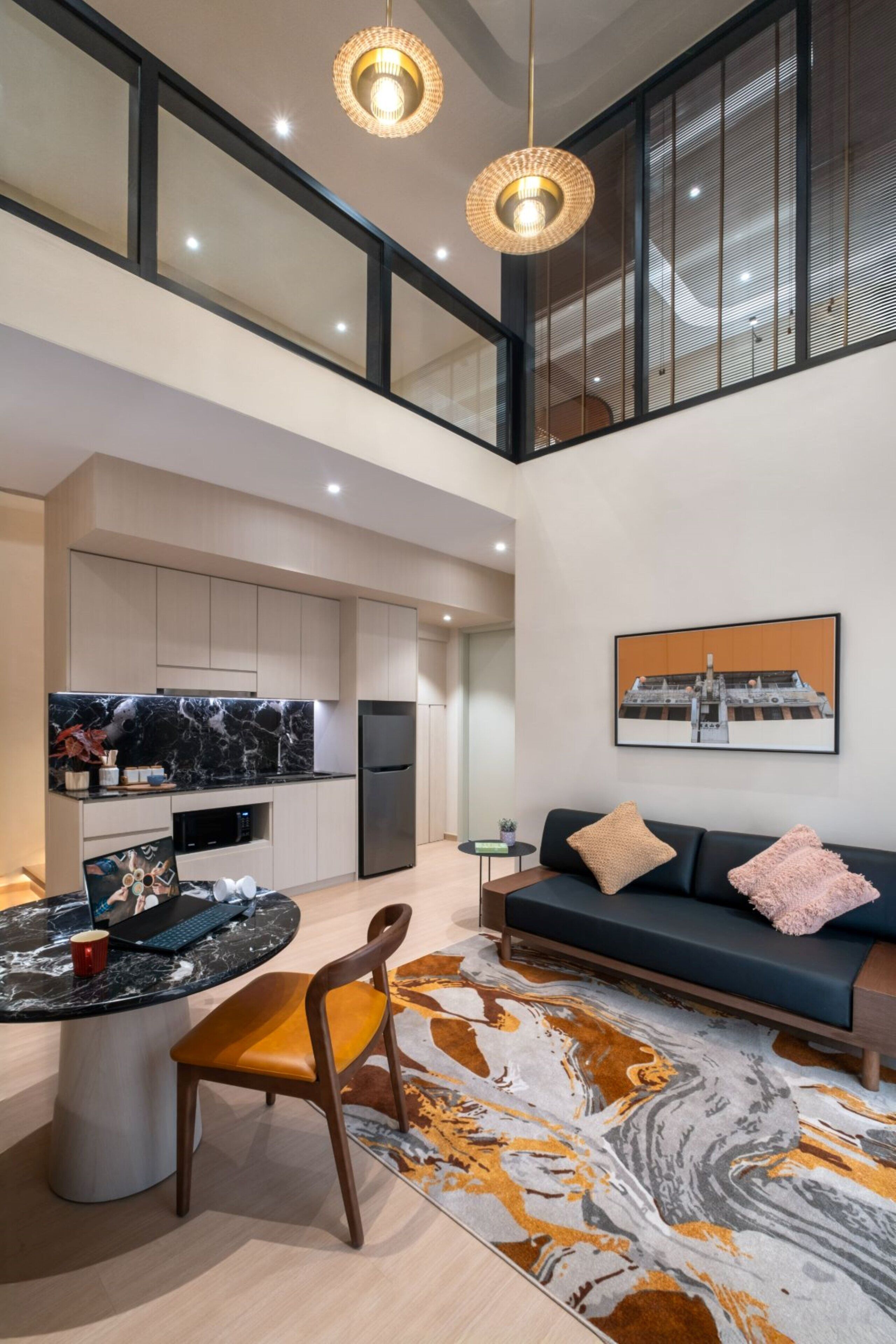 A modern kitchen with a marble countertop, a dining area with a round table and chairs, a sofa with cushions, and a large window with blinds.