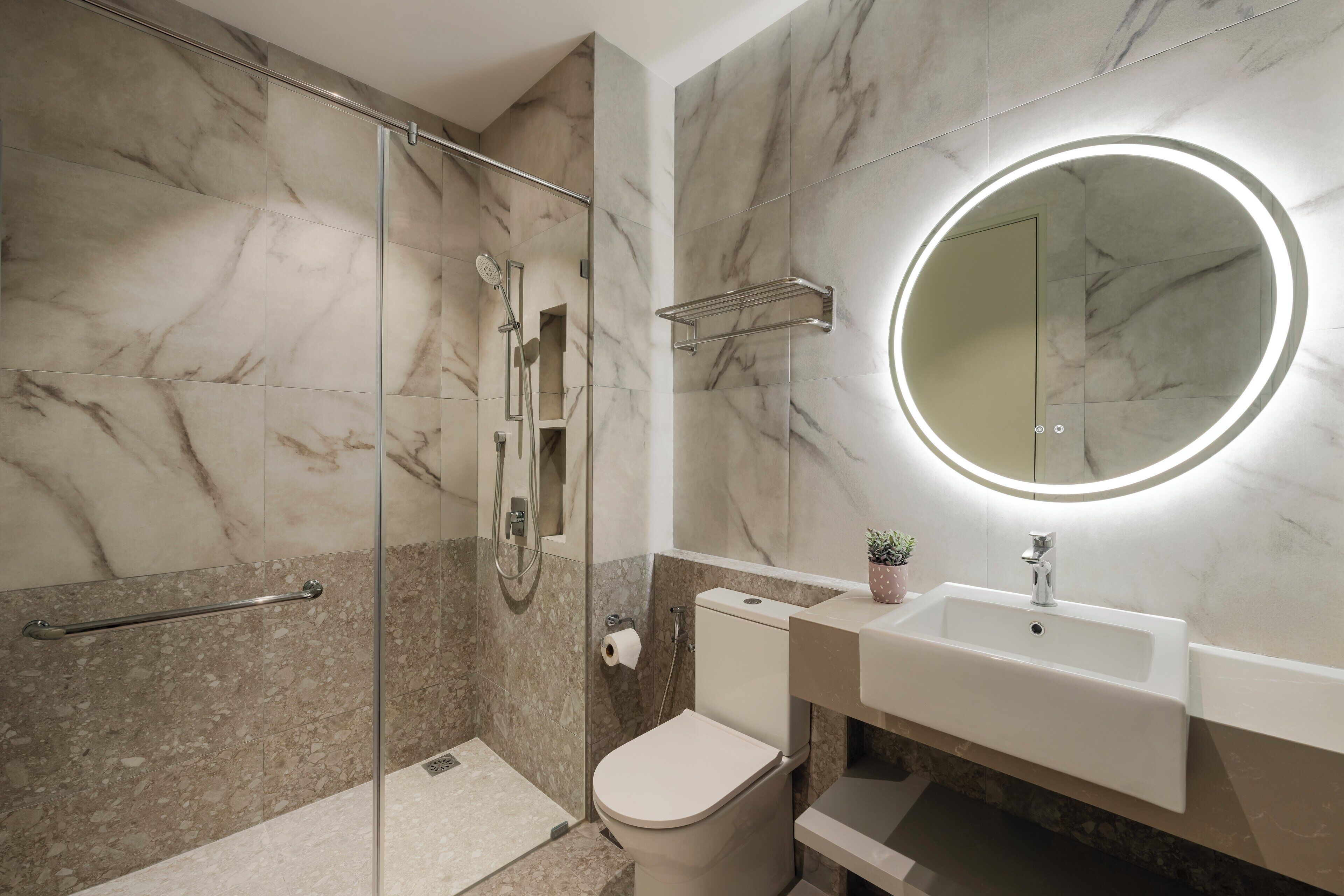 Une salle de bain moderne avec une douche à parois de verre, des toilettes, un lavabo avec un miroir et un pare-baignoire en marbre.