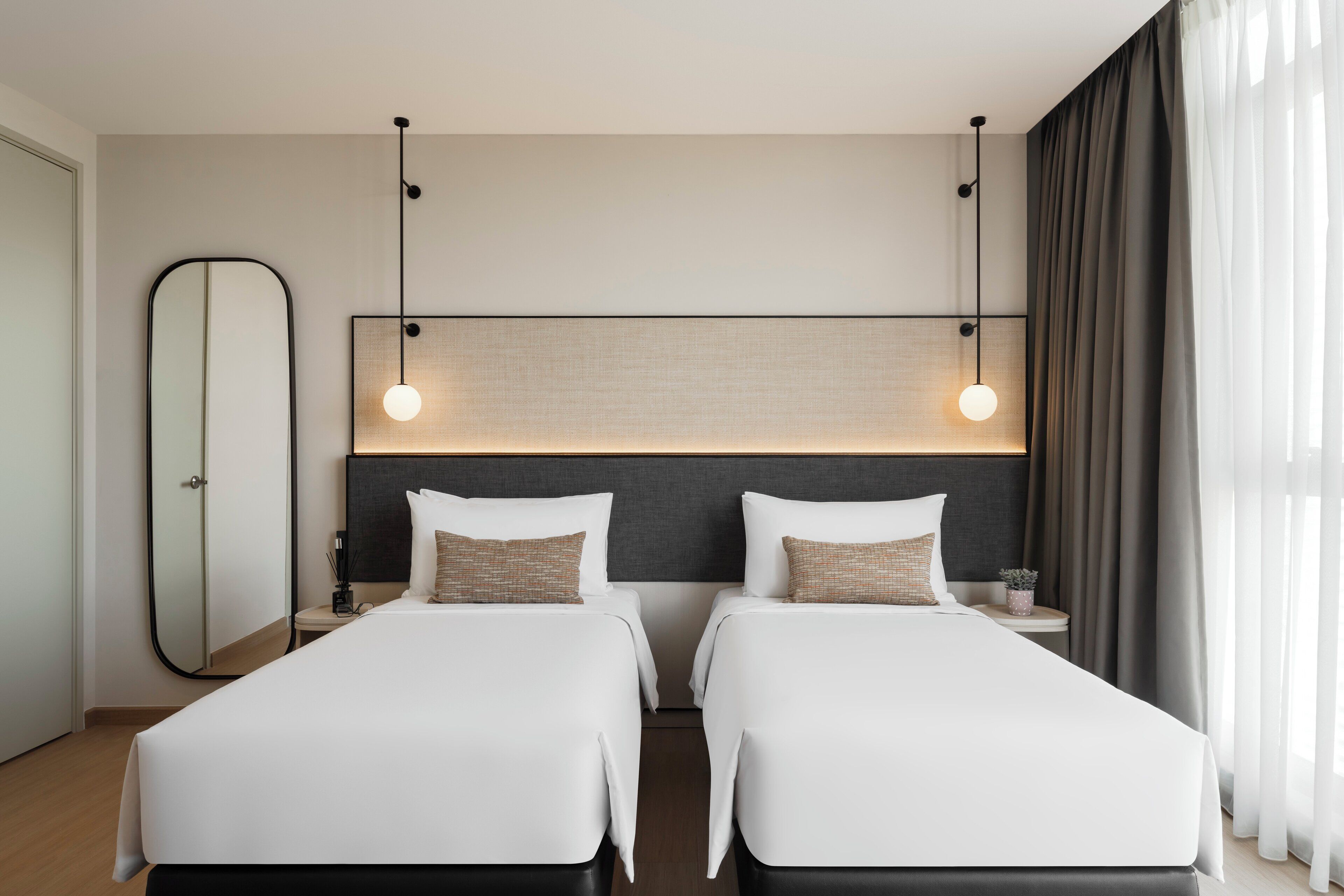 A hotel room with two beds, a large mirror, a nightstand, and a modern light fixture.