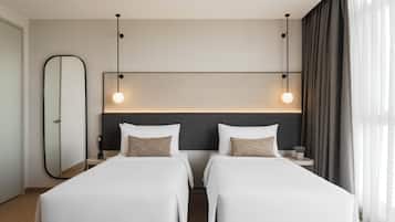 A hotel room with two beds, a large mirror, a nightstand, and a modern light fixture.