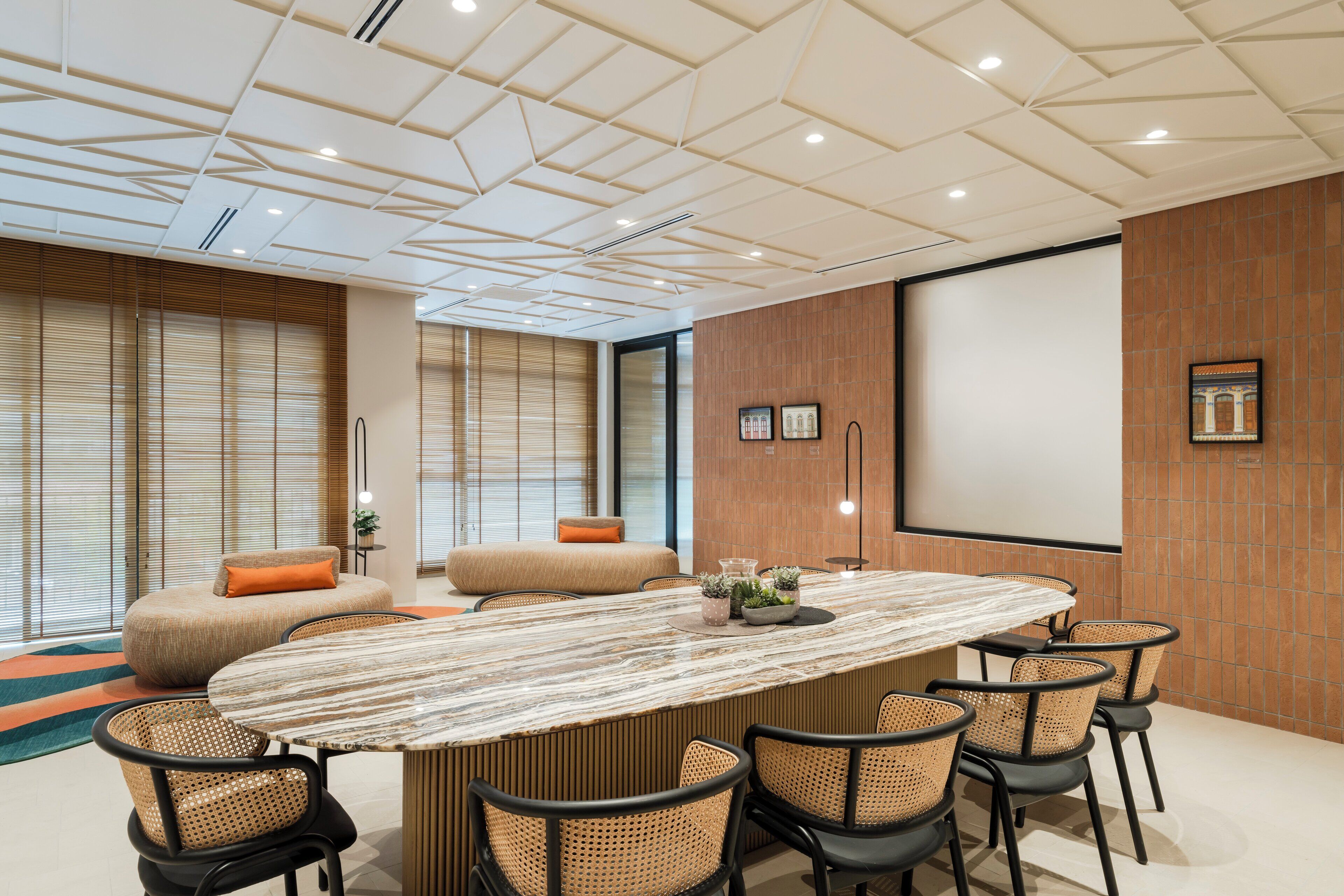 Un salón de conferencias con una gran mesa ovalada, seis sillas, una pantalla de proyector y una pared de madera decorativa.