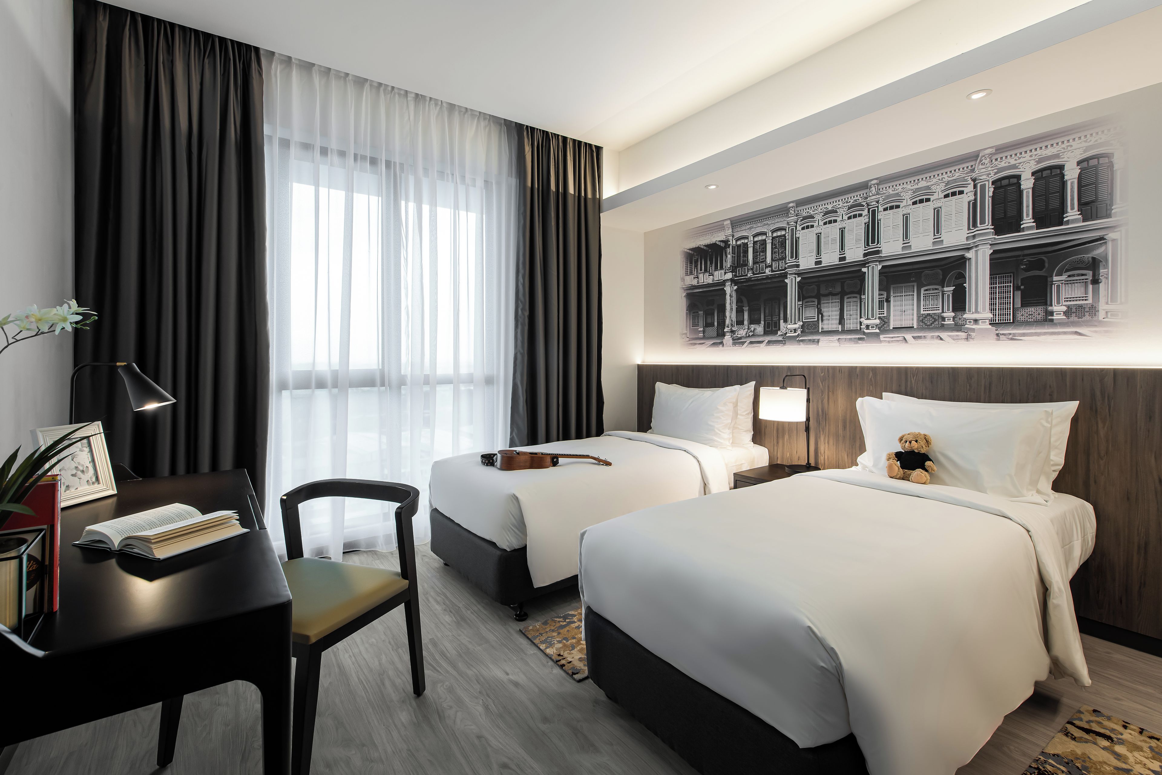 A hotel room with two beds, a desk with a chair, a lamp, and a framed picture on the wall.
