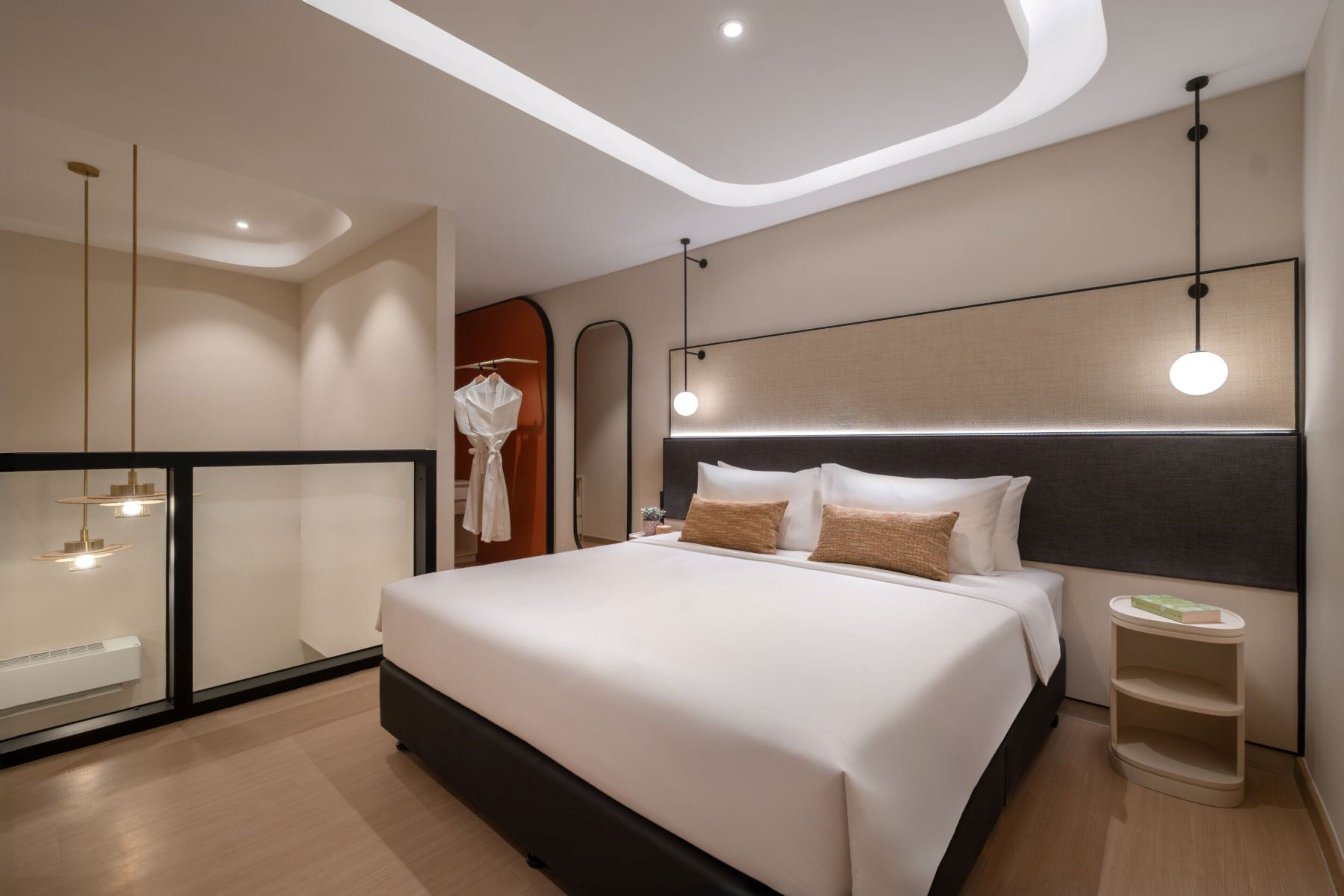 Una habitación de hotel moderna con una cama grande, una mesita de noche, un espejo y un armario.