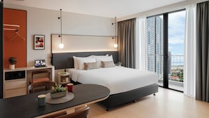 A modern hotel room with a large bed, a desk with a laptop, a dining table, and a view of the city. - Citadines Tanjung Tokong Penang (George Town)