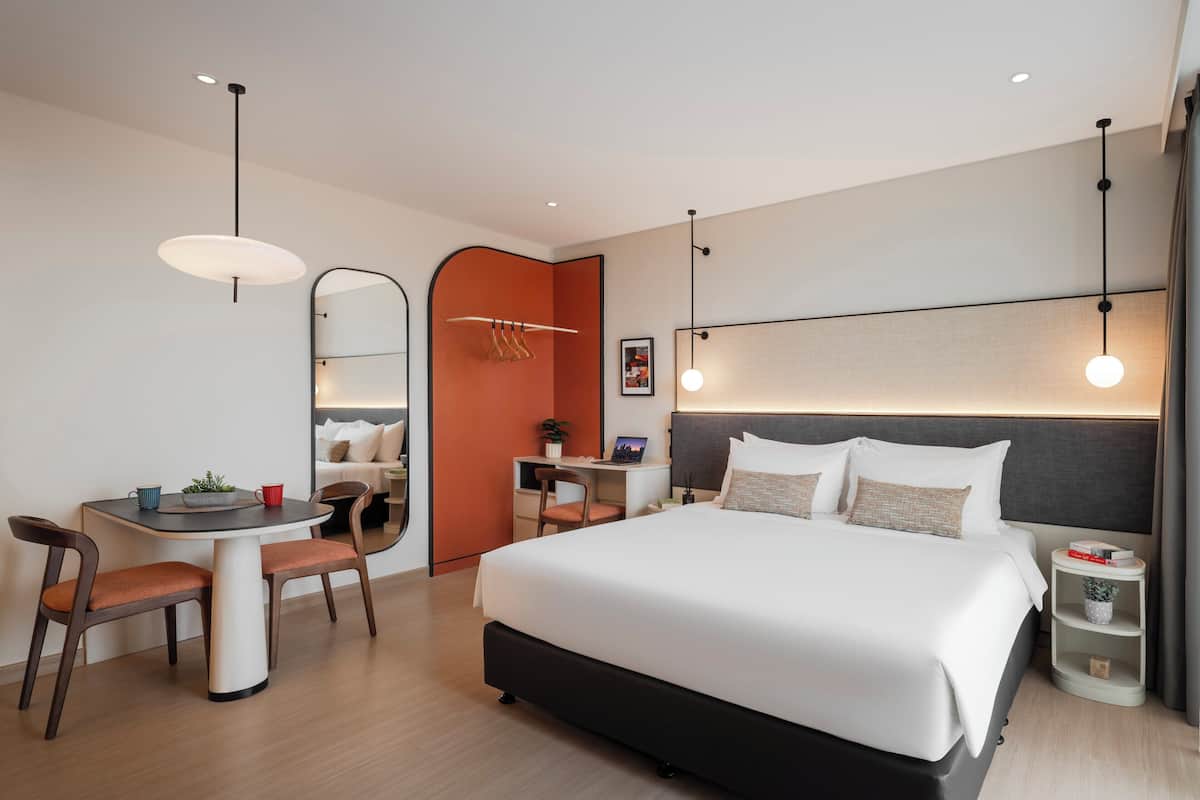 Hotellihuone, jossa on sänky, työpöytä, tuoleja ja peili.