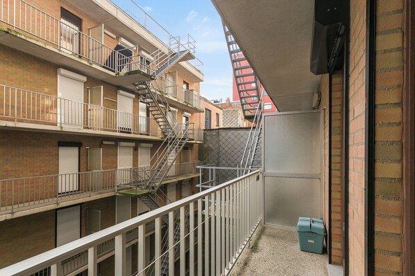 Un edificio de varios pisos con escaleras de emergencia externas, un acceso con rejas y un contenedor de basura.