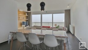 Une chambre d’hôtel moderne dotée d’une grande table à manger, de sièges confortables, d’un téléviseur et offrant une vue sur la ville.