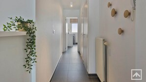 Un couloir étroit avec un radiateur, une plante suspendue et un téléphone fixé au mur.