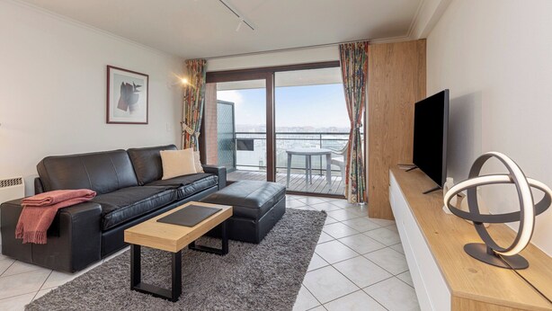 A modern living room with a black leather sofa, a wooden coffee table, and a flat-screen TV on a wooden console. - Apartment in Blankenberge by Marina Views (BLANKENBERGE)