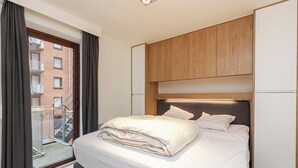 A hotel room with a bed, wooden headboard, and a balcony with a view of a building. - Apartment in Blankenberge by Marina Views (BLANKENBERGE)