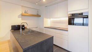 A modern kitchen with a large island, white cabinetry, and a built-in oven. - Apartment in Blankenberge by Marina Views (BLANKENBERGE)