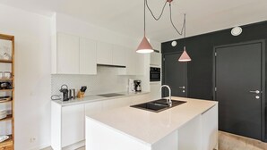 Une cuisine moderne avec des meubles blancs, un îlot central doté d’un évier et des luminaires suspendus.