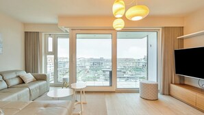 A modern living room with a sofa, a small table, a TV, and a large window with a city view.