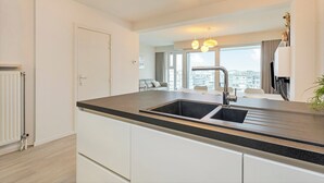 A modern kitchen with a double sink, white cabinetry, and a large window offering a city view.
