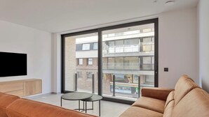 A modern living room with a large sliding glass door, a flat-screen TV, a brown leather sofa, and a small round table.