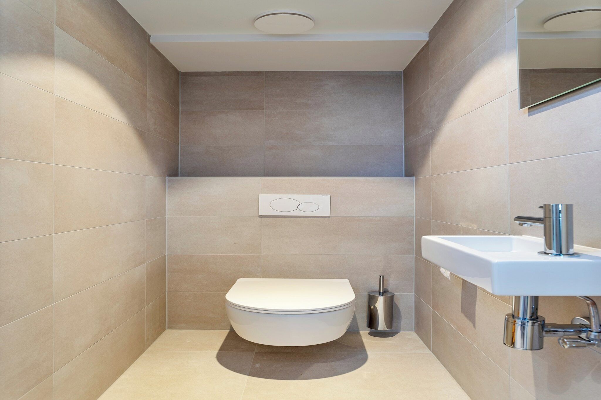 A modern bathroom with a toilet, sink, and a wall-mounted toilet paper holder.