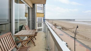 A balcony with a table and chairs, overlooking a beach and a pier. - Apartment in Blankenberge by the Beach (BLANKENBERGE)