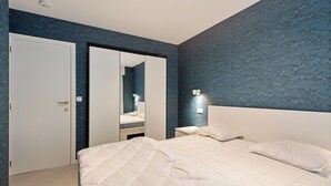 Un dormitorio con dos camas, un armario, un espejo y una mesita de noche con lámpara.