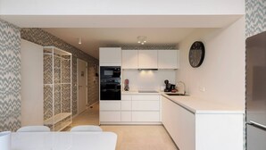 Una cocina moderna con armarios blancos, horno empotrado y microondas. Hay un lavamanos con grifo y un reloj en la pared.