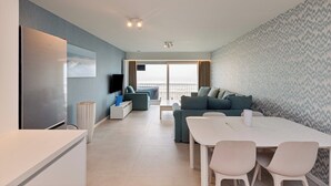 Una sala de estar moderna con un televisor de pantalla plana, una mesa de comedor con sillas, un sofá y un ventanal con vistas.