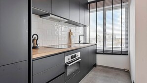 Een moderne keuken met donkere kastjes, een roestvrijstalen afzuigkap, een houten aanrecht en een raam met luxaflex.