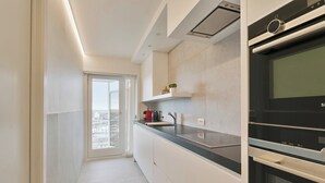 Una cocina moderna con horno empotrado, ventana con vista a la ciudad y encimera con un lavamanos y una pequeña planta.