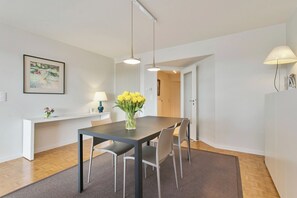 A modern dining area with a dark table, four chairs, a vase of yellow flowers, pendant lights, and a framed picture on the wall. - Flat in Blankenberge with Marina Views (BLANKENBERGE)