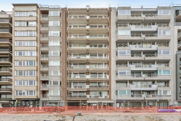 A multi-story apartment building with balconies, a ground-level commercial area, and orange construction fencing. - Flat in Blankenberge with Marina Views (BLANKENBERGE)