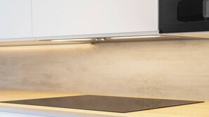 Een keuken met een zwart inductiekookveld op een licht houten aanrecht, witte kasten en een beige achterwand.