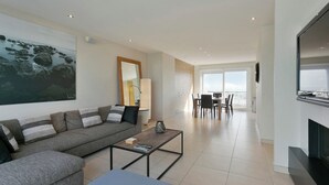 Un salon moderne avec un canapé, une table basse et une cheminée. On aperçoit à l’arrière-plan un coin repas avec des chaises et une table.