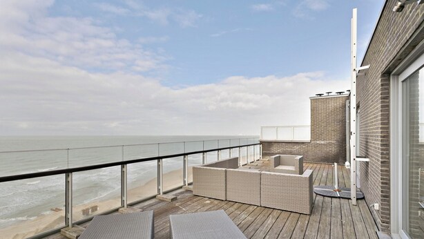 Un balcon doté de meubles en osier, d’une rambarde en verre et offrant une vue sur la mer.