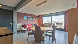Ett modernt hotellrum med en matplats, en röd accentvägg, ett stort fönster med utsikt över staden och en röd gardin.