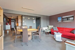 Un soggiorno moderno con un divano rosso, un'area pranzo con un tavolo rotondo e sedie, e una cucina sullo sfondo.